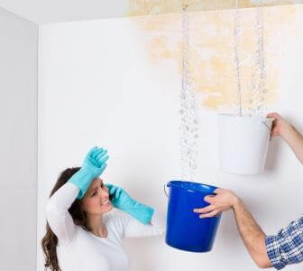 Young Woman Standing With Worker Collecting Water In Bucket From Ceiling In House